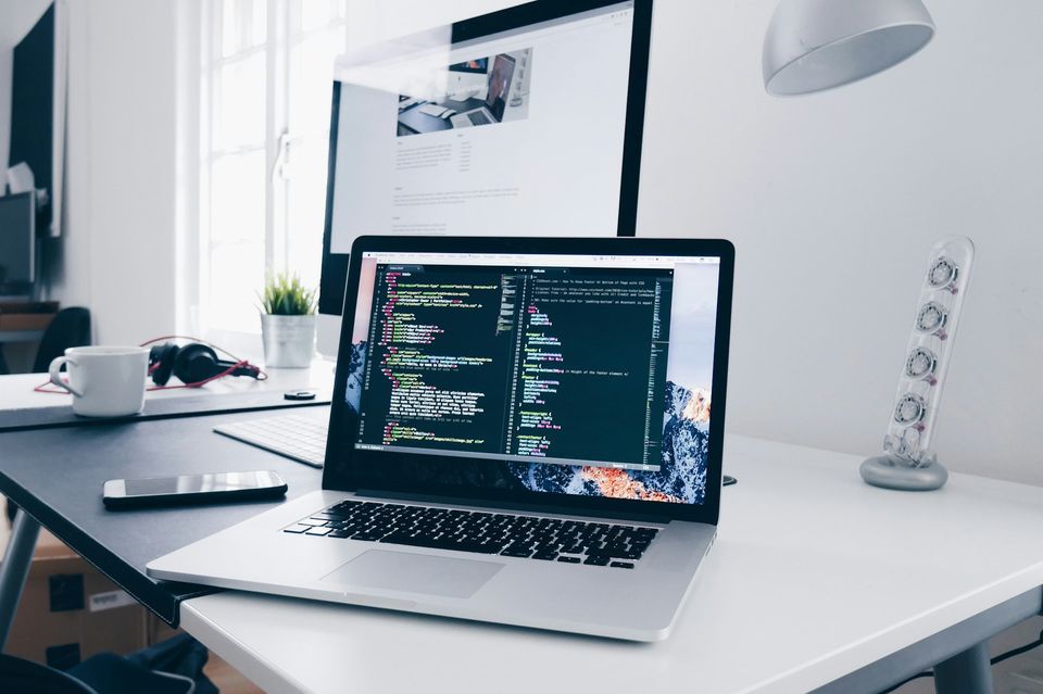 Laptop showing lines of code on a desk beside a desktop monitor